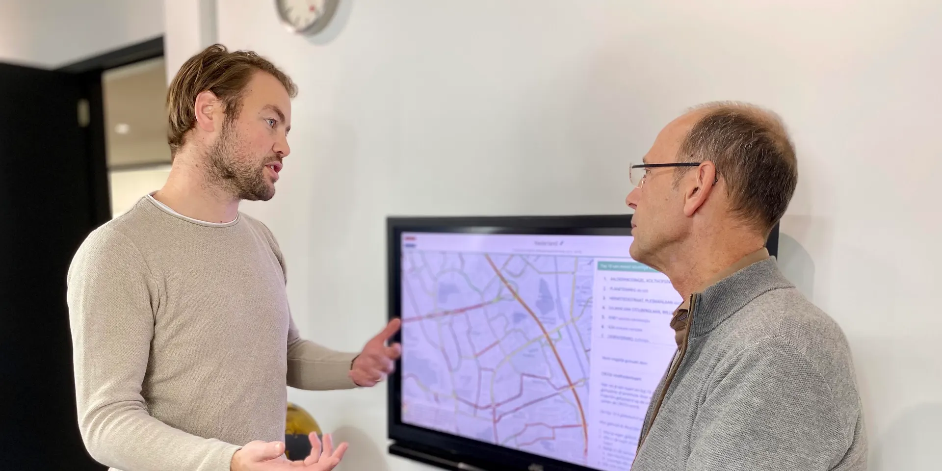 Dos compañeros conversan frente a una pantalla con un mapa de tráfico de su área de actuación.